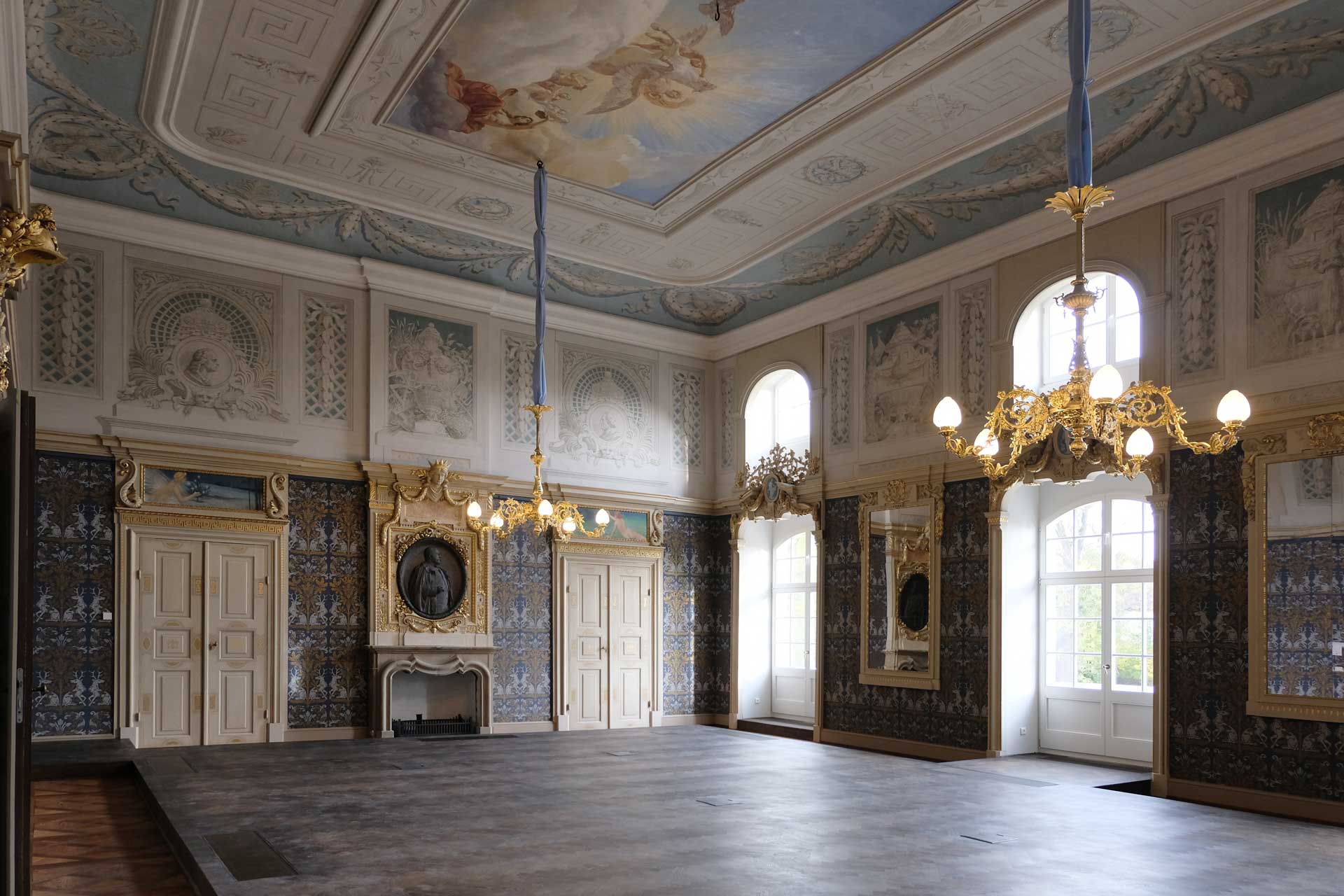 Barockschloss Wachau Innenansicht des weißen Saales, dunkler Parkettboden, Wand- und Deckenmalerei in Blautönen, 2 Candelabras